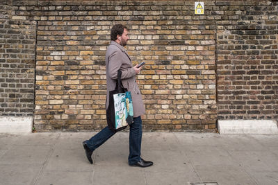 Side view of a young man using mobile phone against brick wall