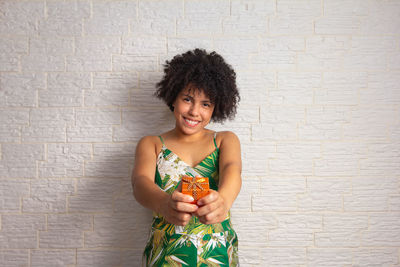 Portrait of smiling woman holding flower against wall