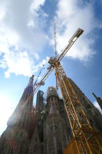 Low angle view of crane by building against sky