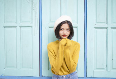 Portrait of young woman standing against door