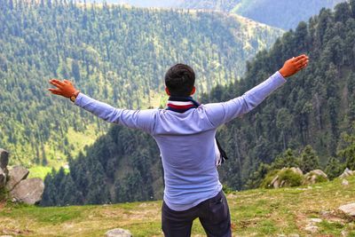 Rear view of man with arms outstretched standing on mountain