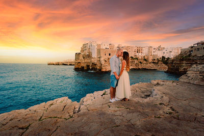 Young couple kissing at sunset in front of the village of polignano a mare