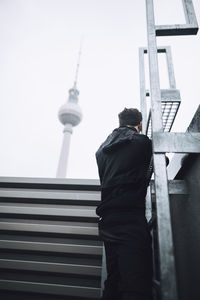 Rear view of man standing by building against sky