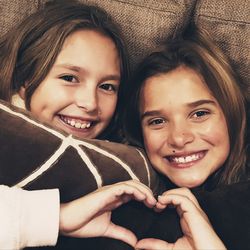 Portrait of smiling sisters forming heart shape at home