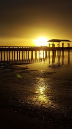 Silhouette bridge over sea against sky during sunset
