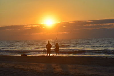 Silhouette men fishing on beach against sky during sunset