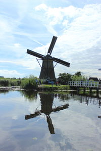 Traditional windmill by lake against sky