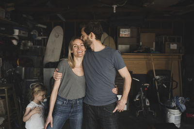 Mid adult man kissing woman by daughter in storage room of house