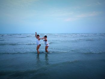Siblings dancing at beach against sky