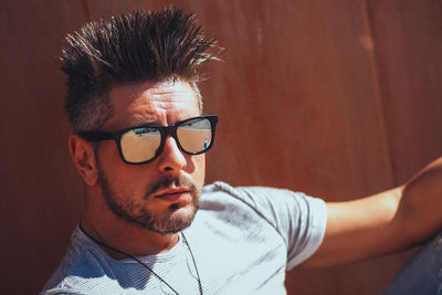 Close-up portrait of handsome man wearing sunglasses against wall