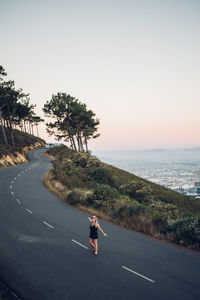 Man on road by sea against clear sky