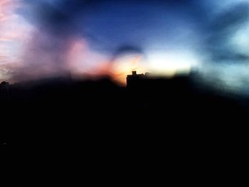 Defocused image of silhouette buildings against sky at sunset