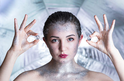 Portrait of young woman with glitters gesturing while holding pearl by face