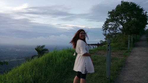 Portrait of happy woman standing on mountain against cloudy sky