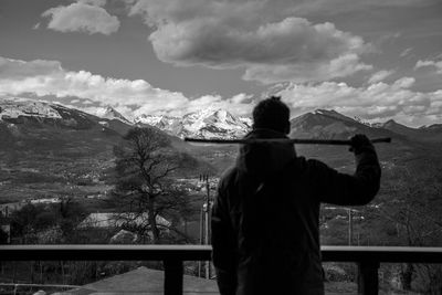 Rear view of man holding stick while standing by railing against sky