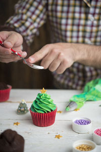 Midsection of man decorating cupcake on table