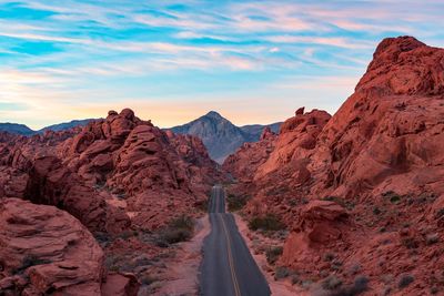 Empty country road amidst rock formations in desert against sky during sunset