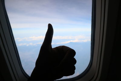 Cropped image of person hand against sky seen through window