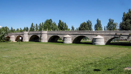 Arch bridge on field against clear blue sky
