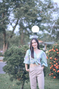 Portrait of smiling young woman standing against trees