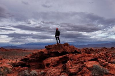 Woman standing on rock formation against cloudy sky