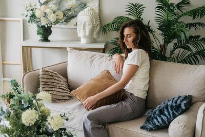 A sad woman sits on a sofa at home hugging a pillow.