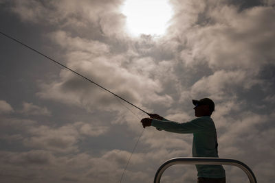 Low angle view of man fishing against cloudy sky