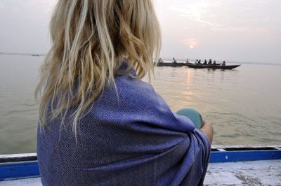 Rear view of woman sitting by sea against sky