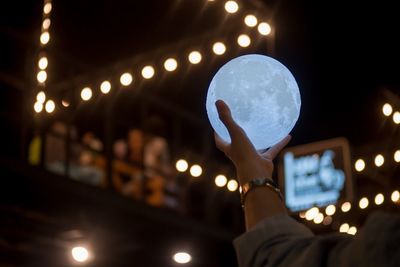 Person holding illuminated light bulb at night