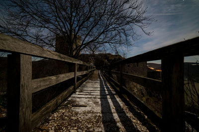 Bridge over footpath amidst bare trees against sky