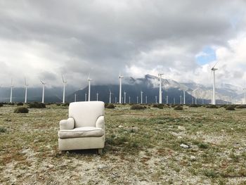 Empty armchair and windmill on landscape against cloudy sky