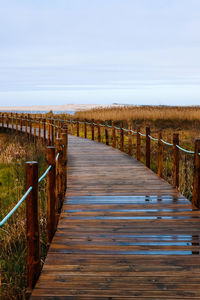 Empty wooden boardwalk leading towards landscape against sky