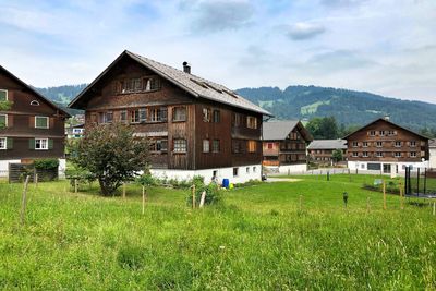 House on field by houses against sky