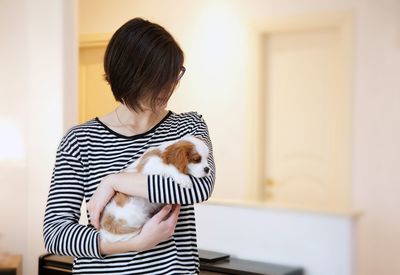 Woman holding puppy while standing at home