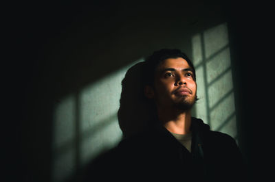 Portrait of young man looking away while standing against wall at home