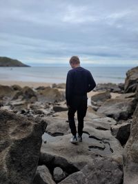 Rear view of man standing on rock against sky