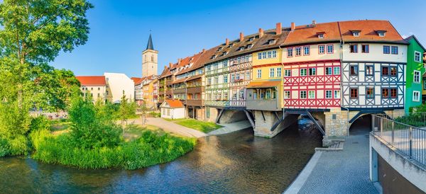 Bridge over river by buildings against sky