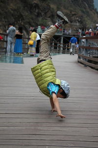 Side view of girl performing handstand on wooden bridge