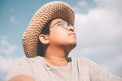 Low angle portrait of man wearing hat against sky