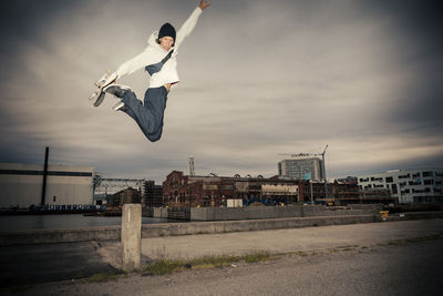 Mid adult man with skateboard jumping against sky
