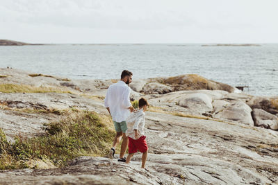 Rear view of father and son walking towards sea on rocky land