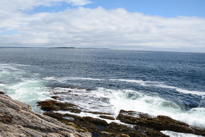 Scenic view of sea with surf crashing on the rocks against sky