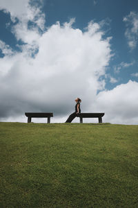 Young woman relaxing on a park bench ,with green grass ,blue sky and cloud