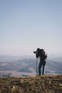 Rear view of man photographing from mountain against clear sky