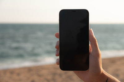 Cropped hand of woman holding mobile phone at beach