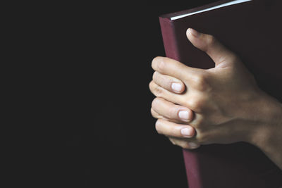 Close-up of hand holding book against black background