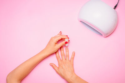 Woman's hand while taking care of her nails on pink background, flat lay