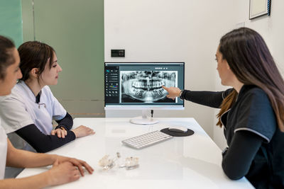 Dentist discussing with nurses over x-ray in computer at office