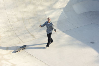 Portrait of man with skateboard walking on ramp in park