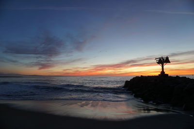 Silhouette beach against sky during sunset